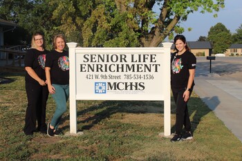 Three female MCHHS employees standing outside, next to Senior Life Enrichment sign.